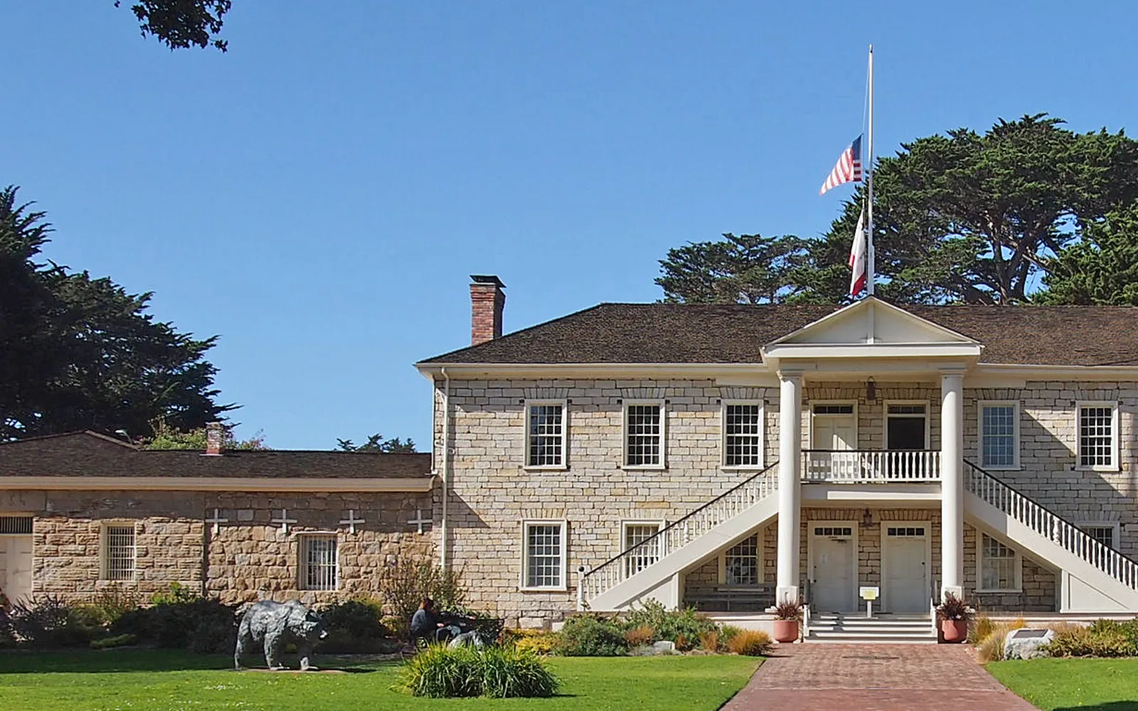Colton Hall, a historic adobe building with white walls and dark wooden doors and windows, with the old Monterey Jail visible beside it